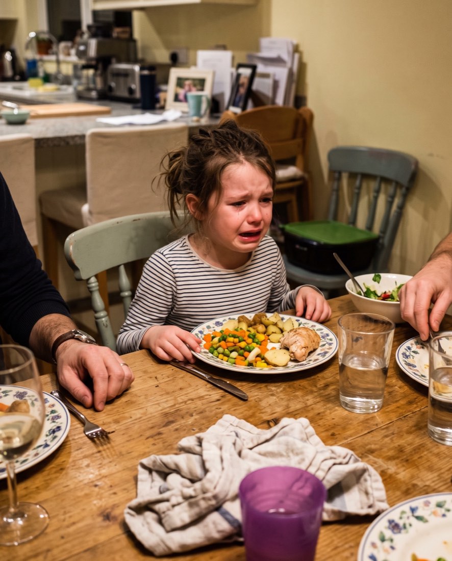 A girl crying suddenly at the dinner table with a full plate in front of her